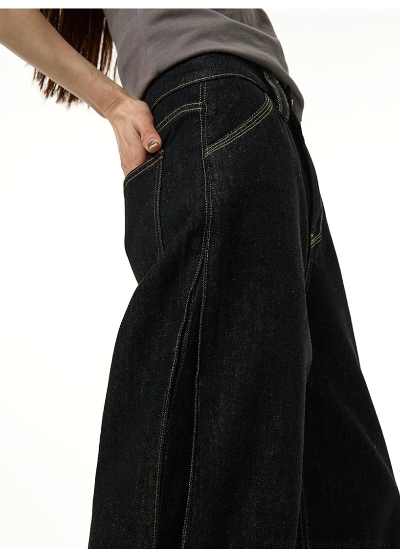 Three-quarter side close-up of black wide-leg jeans showing asymmetrical seams, contrast yellow topstitching, hip construction, and classic pocket details