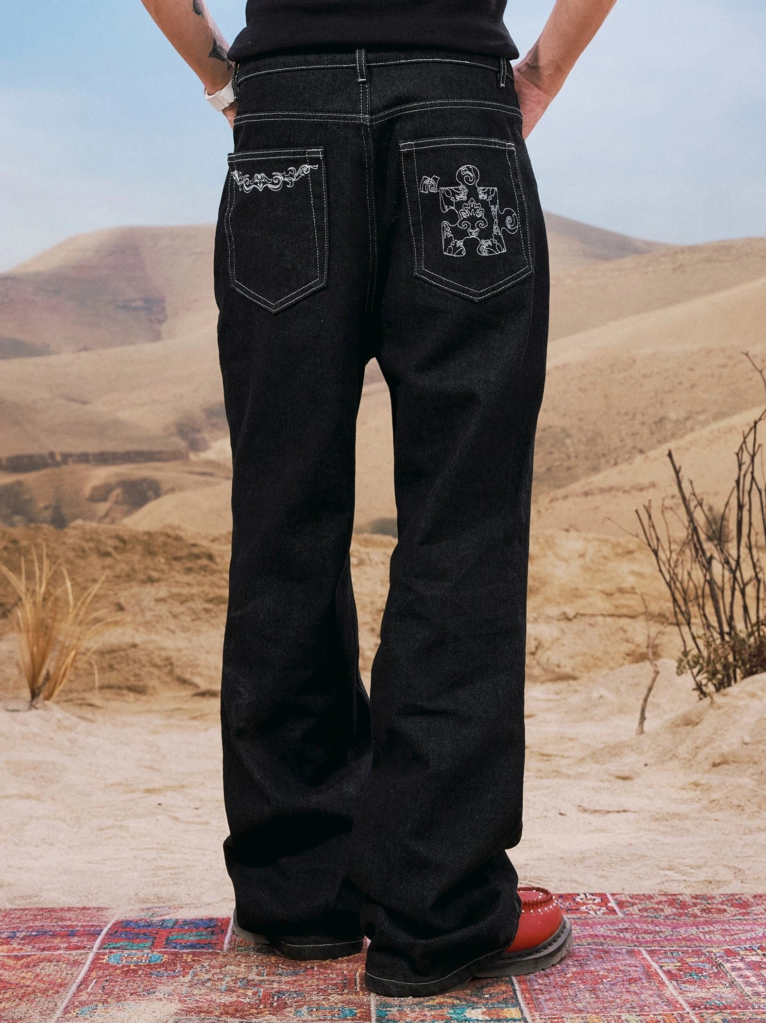 Back view of men's black wide leg jeans showing decorative embroidered back pockets and elongated stacked denim fit