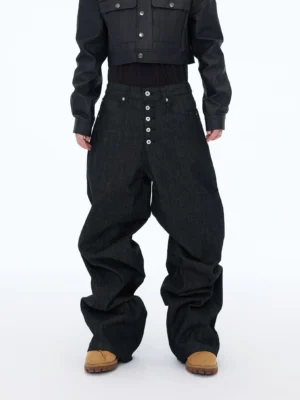 Front full-body view of oversized black wide leg jeans with exposed five-button fly, puddle-length stacked hem, rigid denim, cropped leather jacket, and tan work boots