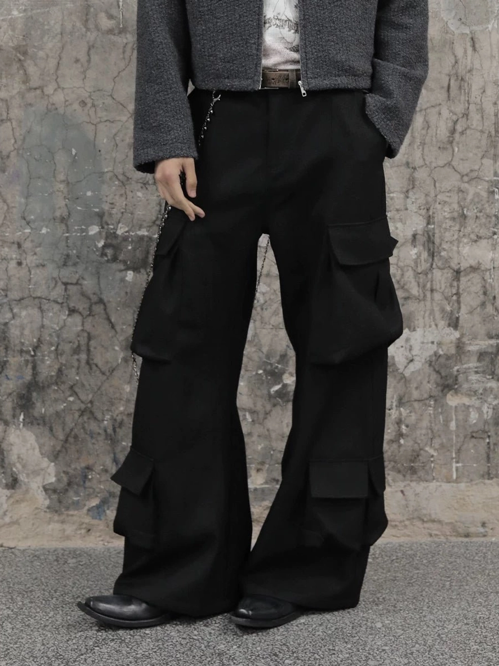 Black wide-leg multi-pocket cargo trousers styled with a grey cropped jacket and leather shoes in an industrial streetwear setting