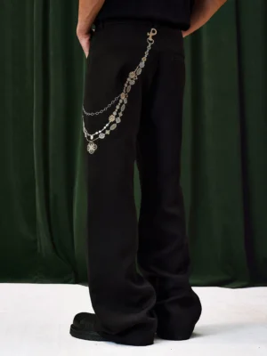 Side view of black wide-leg pants with layered jeweled hip chain, buttoned trouser waist, elongated leg, and black leather shoes
