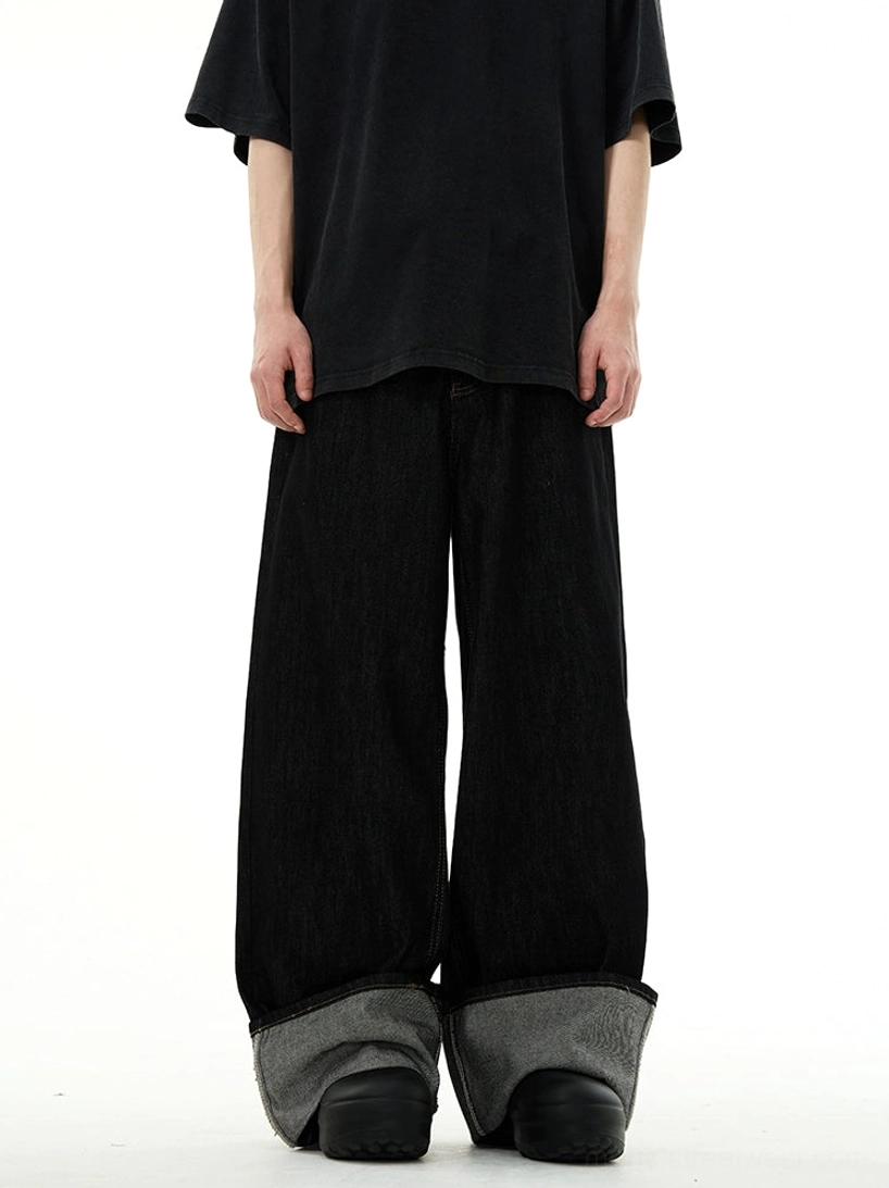Front full-body view of black extra-long wide-leg denim jeans with contrasting grey reverse rolled cuffs
