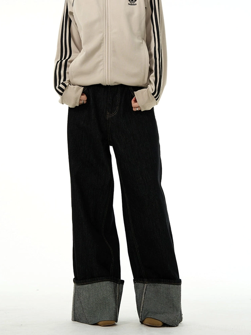 Three-quarter side view of black wide-leg straight denim jeans with oversized rolled hems and beige track jacket styling