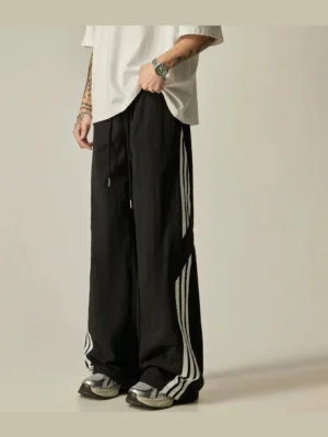Black wide-leg side stripe track pants for Korean streetwear shown in a front three-quarter studio view with white double stripes and drawstring waist