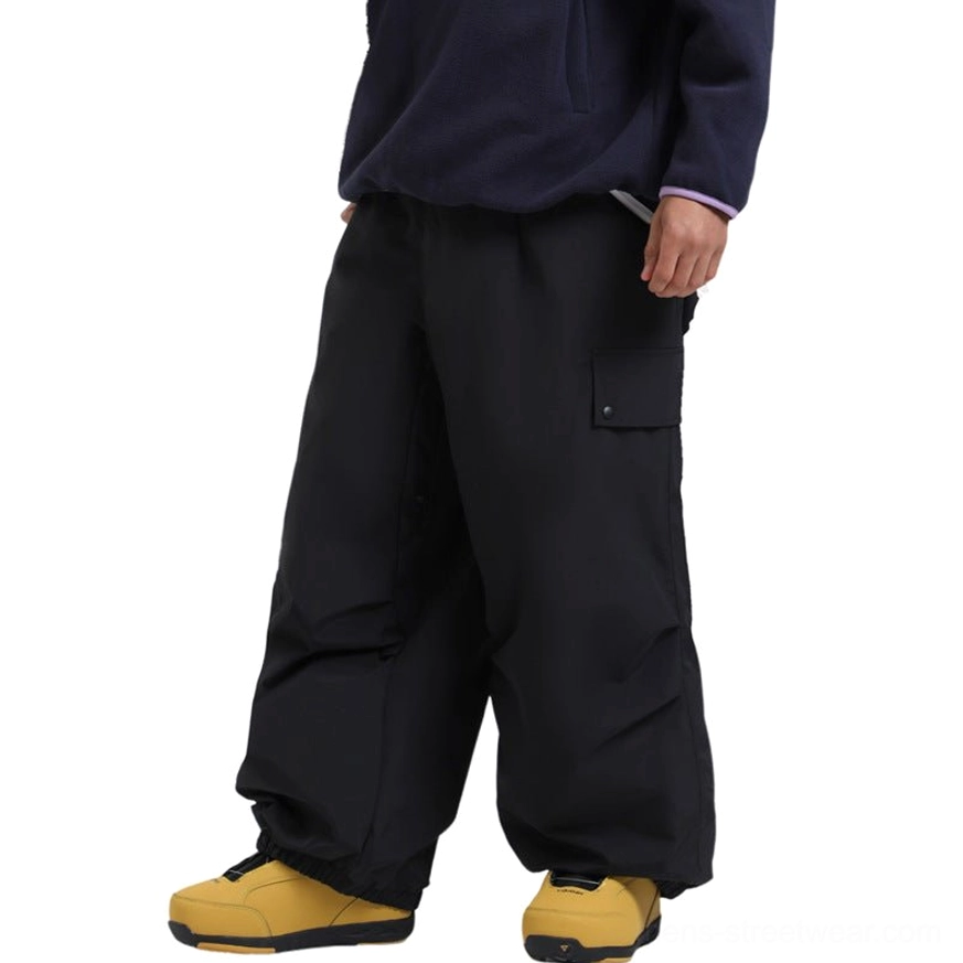 Black wide-leg ski cargo pants shown from the side with streamlined outdoor silhouette, thigh flap cargo pocket, elasticated cuffs, and technical snow shell