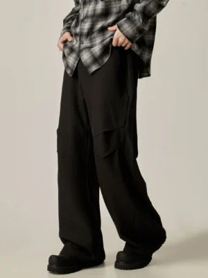 Black wide-leg streetwear cargo trousers shown from a front three-quarter angle with asymmetrical side pockets and fluid fabric drape
