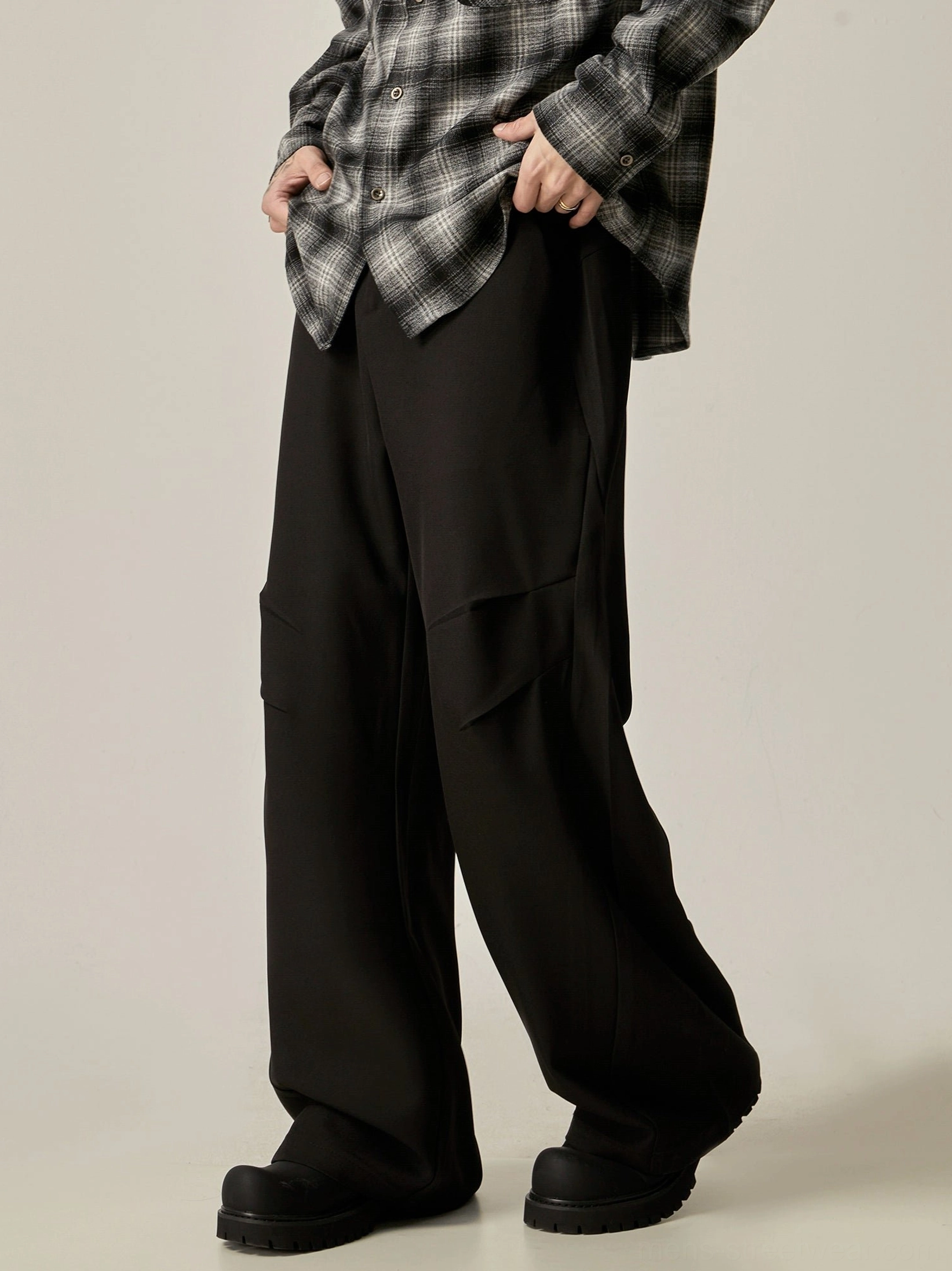 Black wide-leg streetwear cargo trousers shown from a front three-quarter angle with asymmetrical side pockets and fluid fabric drape