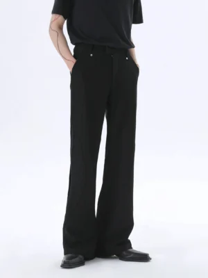 Front three-quarter view of black wide-leg tailored trousers with curved seams, high-rise waist, metal hardware, front pockets, and relaxed streetwear fit