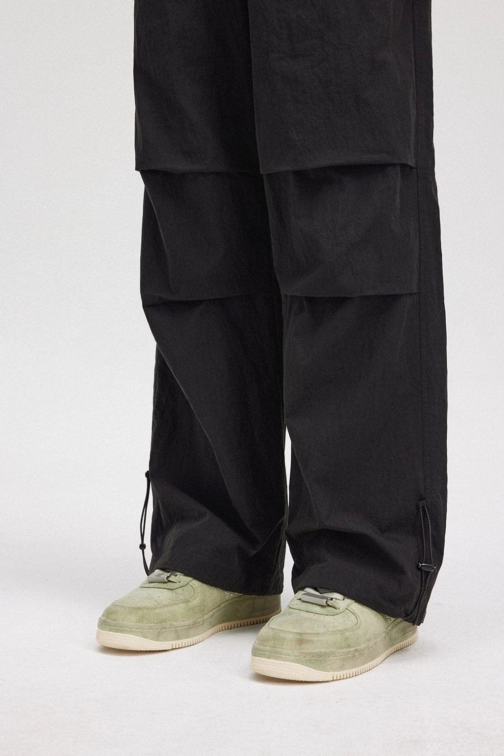 Close-up view of black wide-leg track pants ankle with adjustable drawstring hem and pleated panel construction