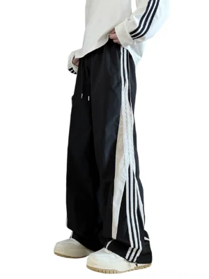 Black wide-leg track pants with triple white side stripes shown in a left-side full body streetwear outfit view