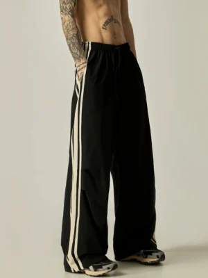 Black wide-leg triple stripe nylon track pants with off-white side stripes and adjustable drawstring waistband front view