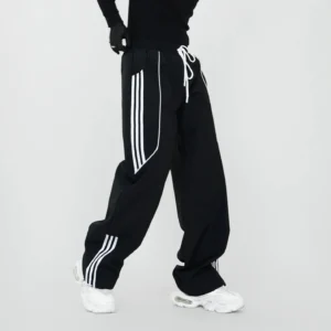 Black wide-leg triple-stripe track pants with elastic drawstring waist, loose Korean streetwear silhouette, and white side stripes styled with chunky sneakers
