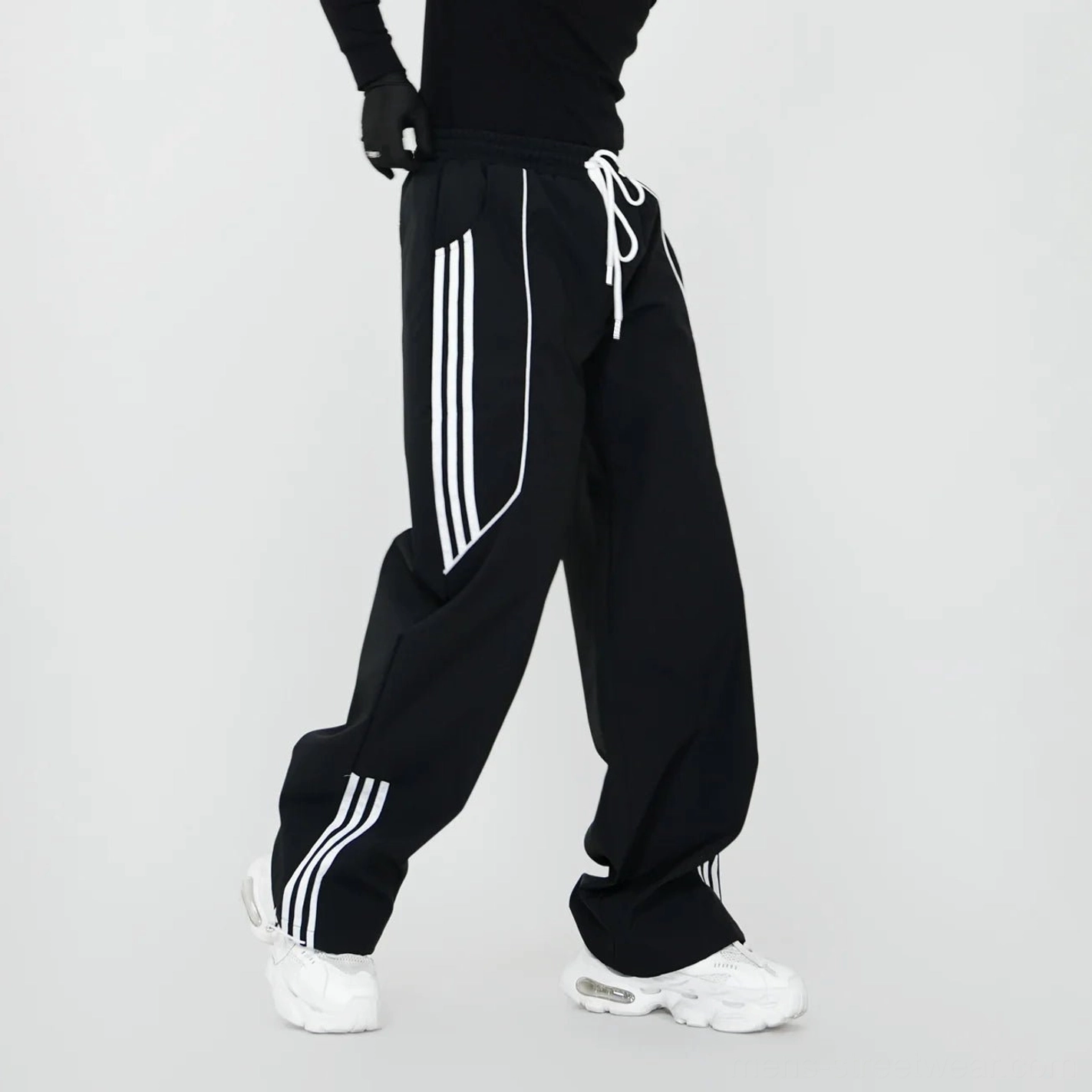 Black wide-leg triple-stripe track pants with elastic drawstring waist, loose Korean streetwear silhouette, and white side stripes styled with chunky sneakers
