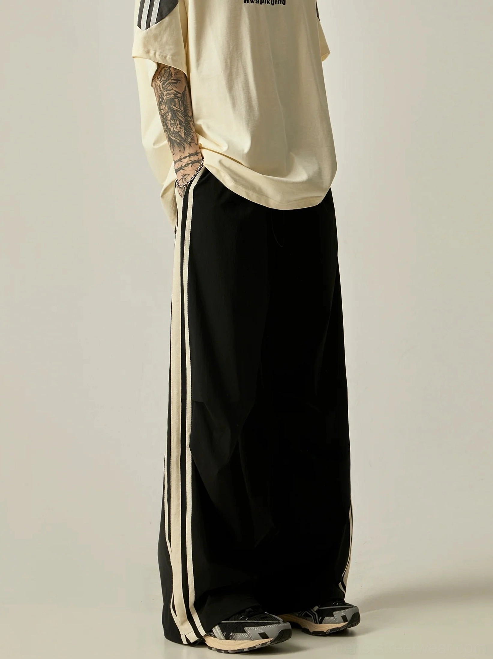 Side view of black wide-leg triple stripe track pants showing relaxed drape, long hem, and contrast side stripes