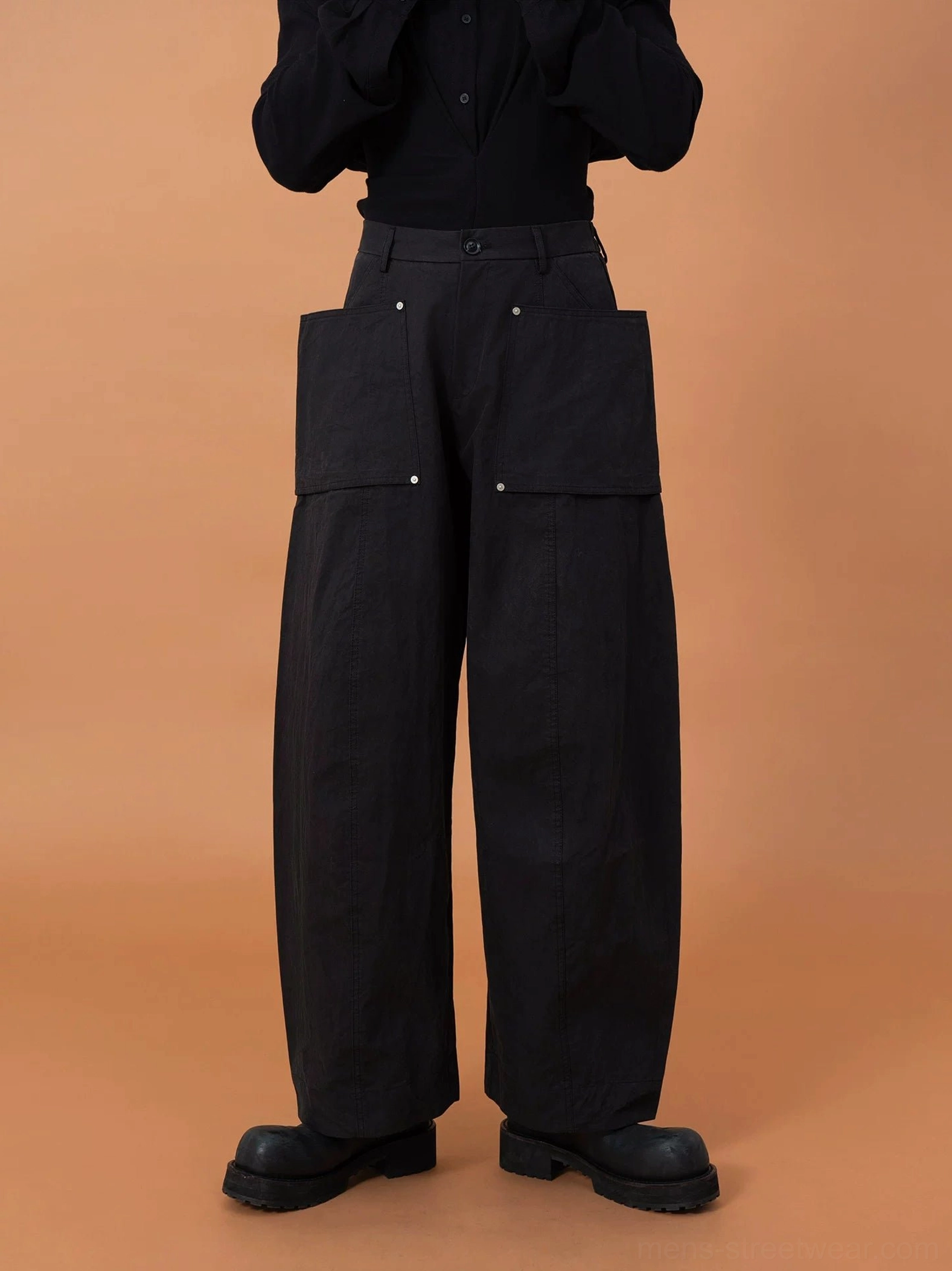 Front view of black wide-leg utility cargo pants featuring oversized patch pockets, industrial metal rivets, and a relaxed urban fit