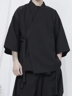 Close-up front view of black wrap kimono shirt showing crossover collar, self-tie waist straps, loose three-quarter sleeves, and matte black fabric