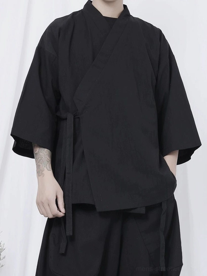 Close-up front view of black wrap kimono shirt showing crossover collar, self-tie waist straps, loose three-quarter sleeves, and matte black fabric