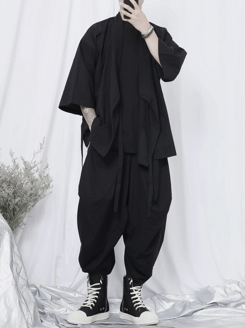 Side profile of black wrap kimono shirt layered over a basic tee with loose sleeves, hanging side straps, and relaxed harem pants