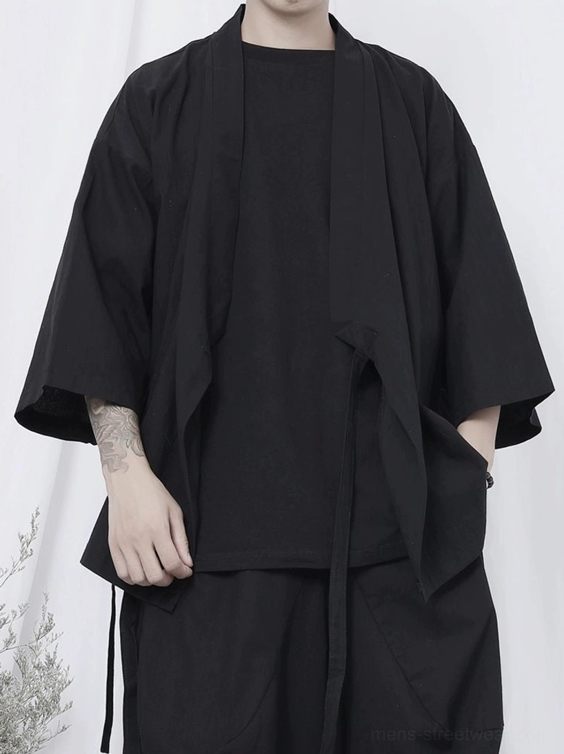 Close-up black wrap kimono shirt showing crossover front, self-tie side straps, matte fabric texture, and oversized relaxed cut