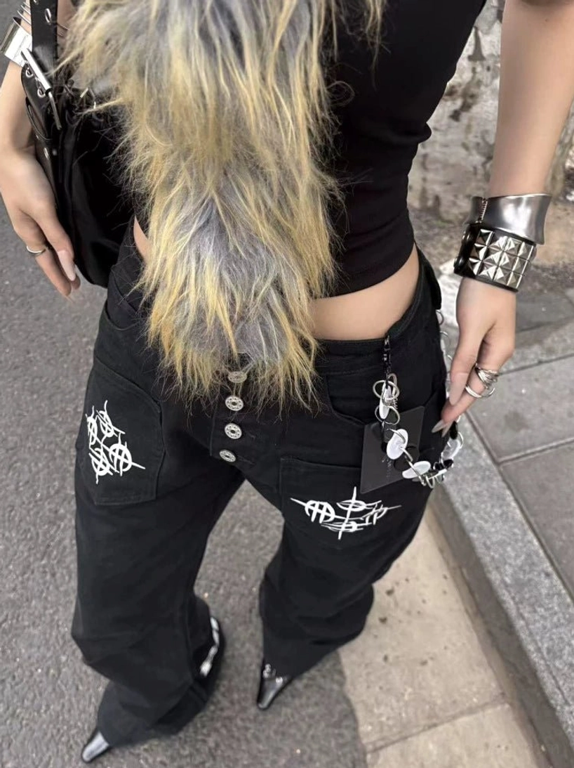 Close-up of black Y2K flare jeans showing the multi-button fly, tribal front pocket graphics, and metallic waist chain styling