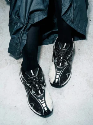 Black and white Yin-Yang tech runner sneakers worn with dark streetwear outfit in urban concrete setting