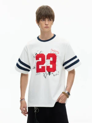 Front half-body view of white Blood Tour 23 varsity graphic T-shirt with navy ribbed neckline, double sleeve stripes, and distressed red 23 streetwear print