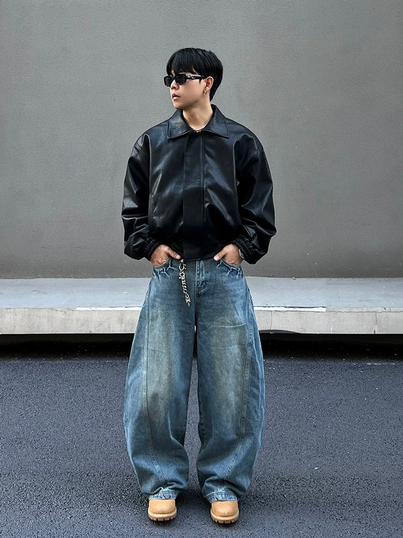 Medium front view of oversized blue streetwear jeans with faded thigh details, curved side seam, metal chain waist accessory, sunglasses, and tan work boots