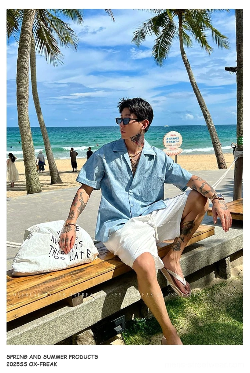 Blue crinkled seersucker Cuban collar shirt shown from the side while seated on a seaside wooden bench