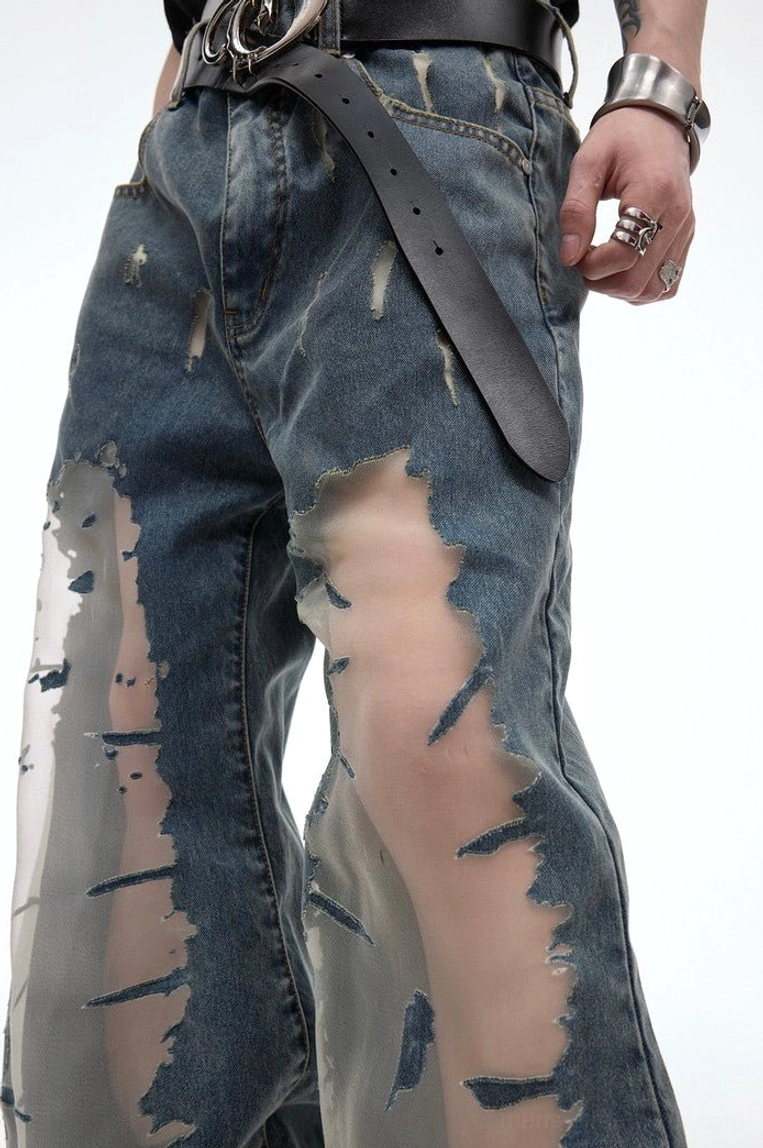 Close up detail of distressed blue denim jeans showing frayed thigh openings with semi transparent mesh inserts and vintage fading