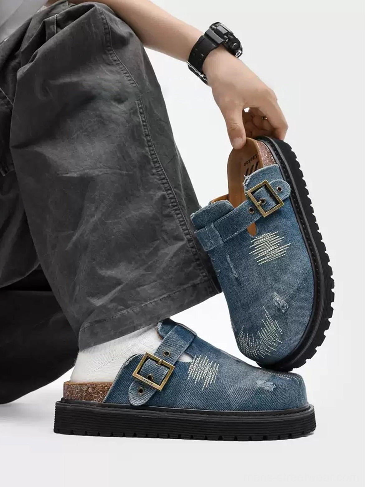 Side view of blue distressed denim mule clogs worn with dark gray cargo pants and white socks, showing the rugged platform outsole