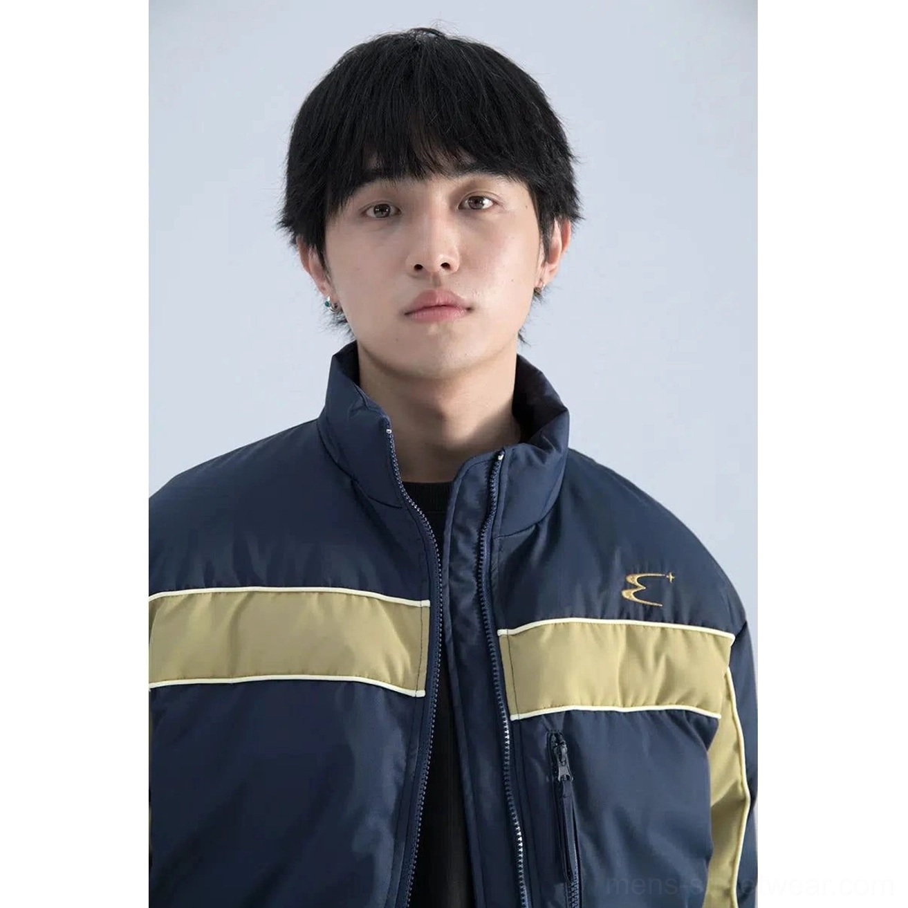 Close-up of blue and khaki color block puffer jacket showing stand collar embroidered chest detail and front zipper pocket