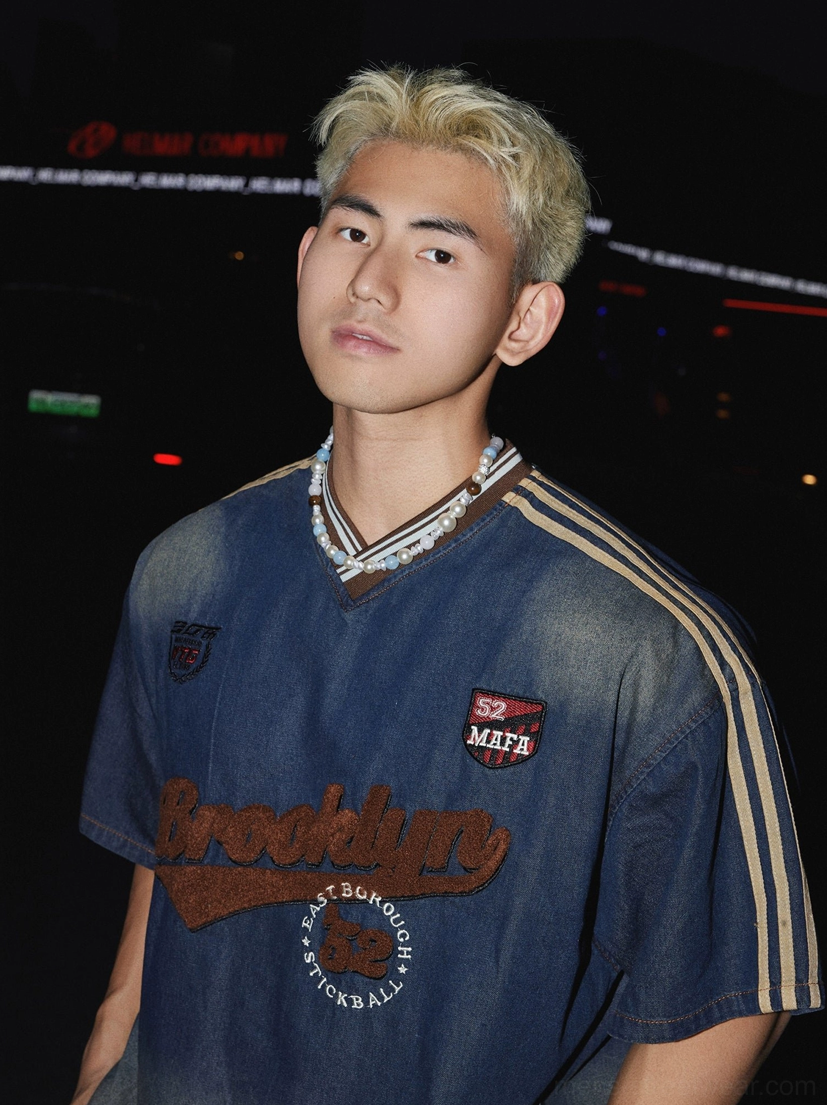 Upper front detail of vintage blue ombre denim streetwear T-shirt featuring embroidered Brooklyn lettering, ribbed V-neck, varsity patches, and layered necklace styling