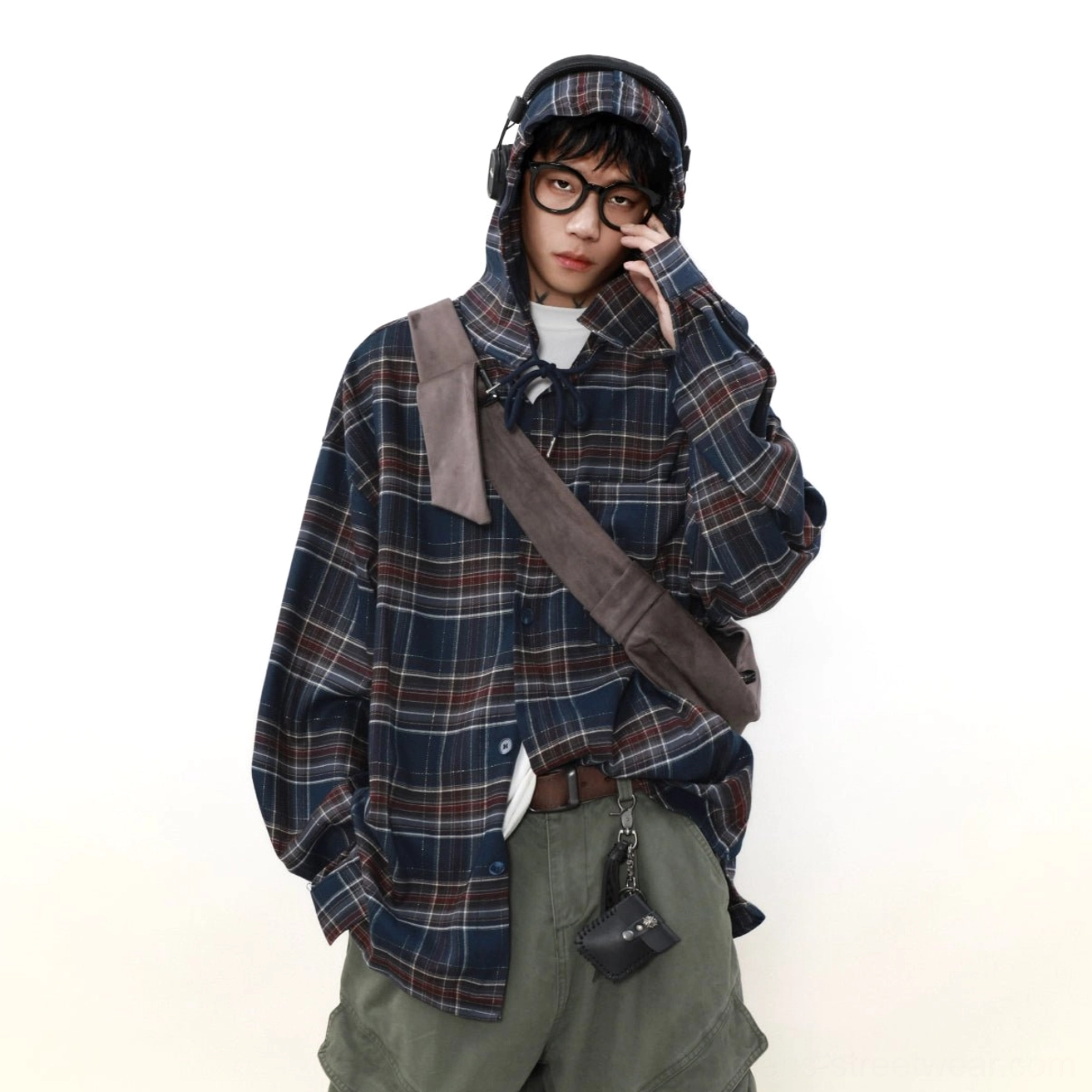 Three-quarter view of a male model in an oversized blue and red checkered hooded shirt with crossbody strap and small waist pouch