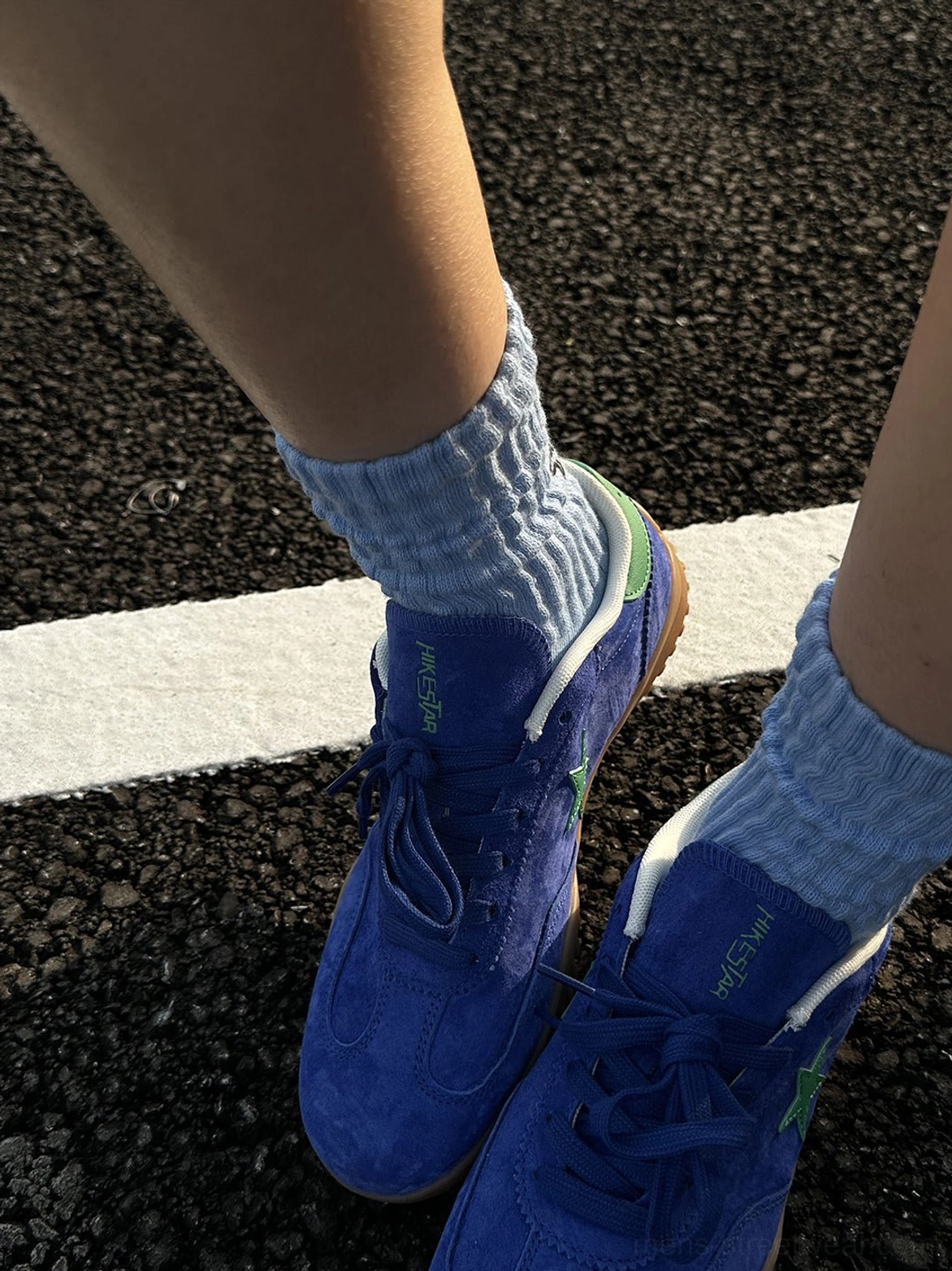 Top-down view of both blue suede star embroidered trainers with matching ribbed light blue socks, white laces, and gum rubber soles