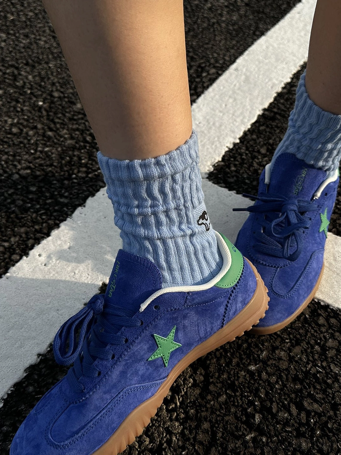 Rear side view of blue suede star trainers showing green five point star embroidery, green heel tabs, white padded collar trim, and gum soles