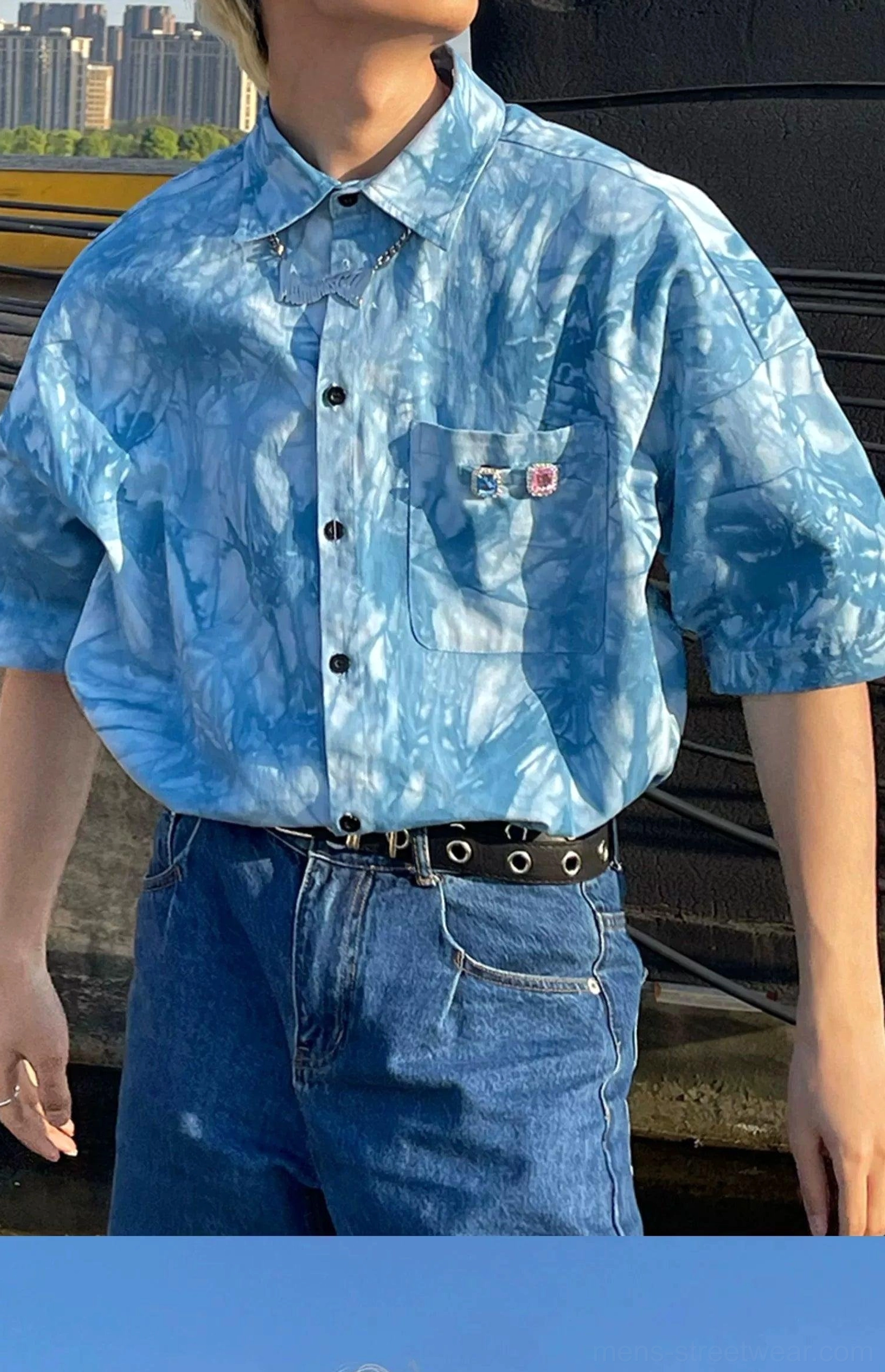 Male model wearing a tucked blue tie-dye button-up streetwear shirt with denim jeans and black eyelet belt