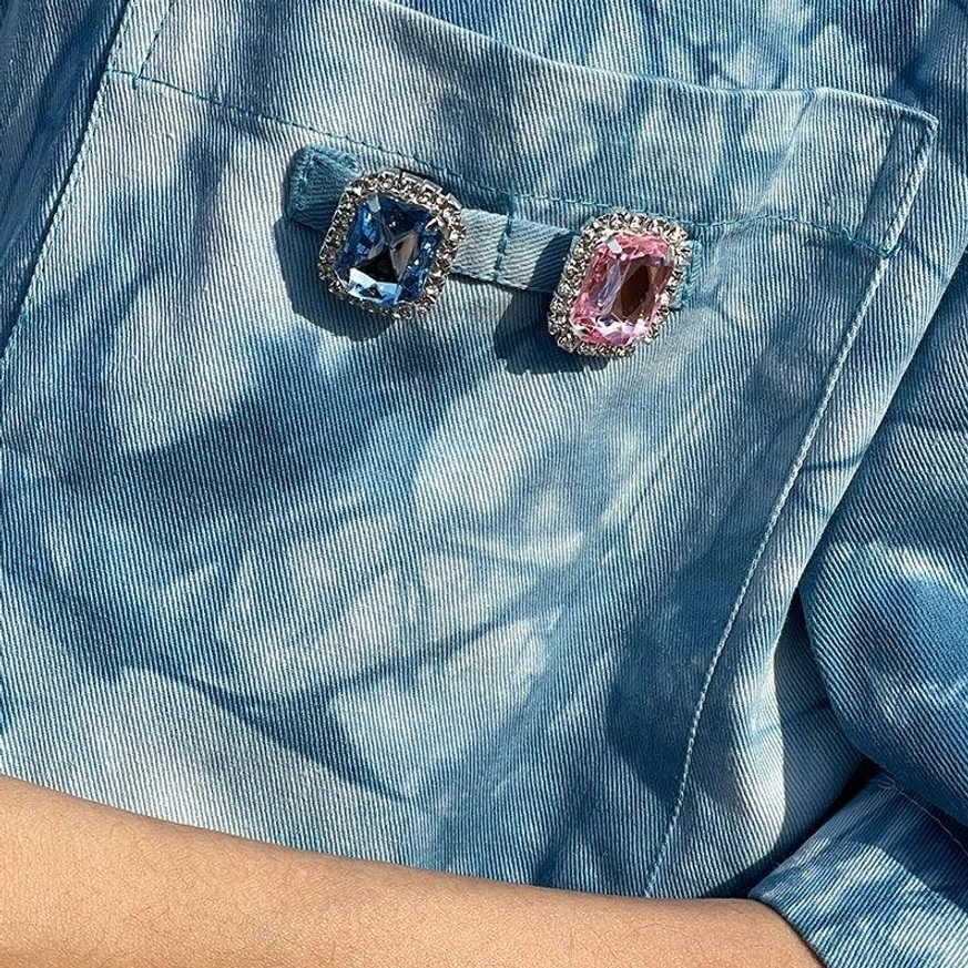 Close-up of blue tie-dye cotton shirt chest pocket with decorative buckles and blue pink gemstone-style accents