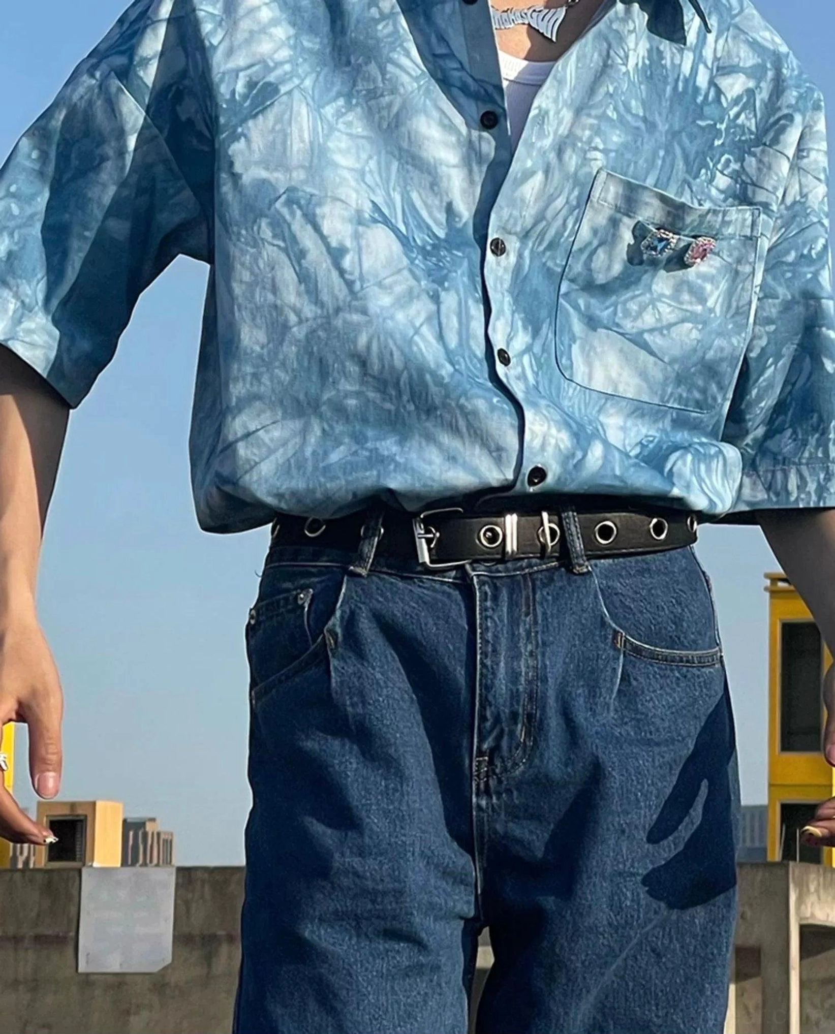 Waist-down styling view of a tucked blue tie-dye streetwear shirt with denim jeans and black eyelet belt