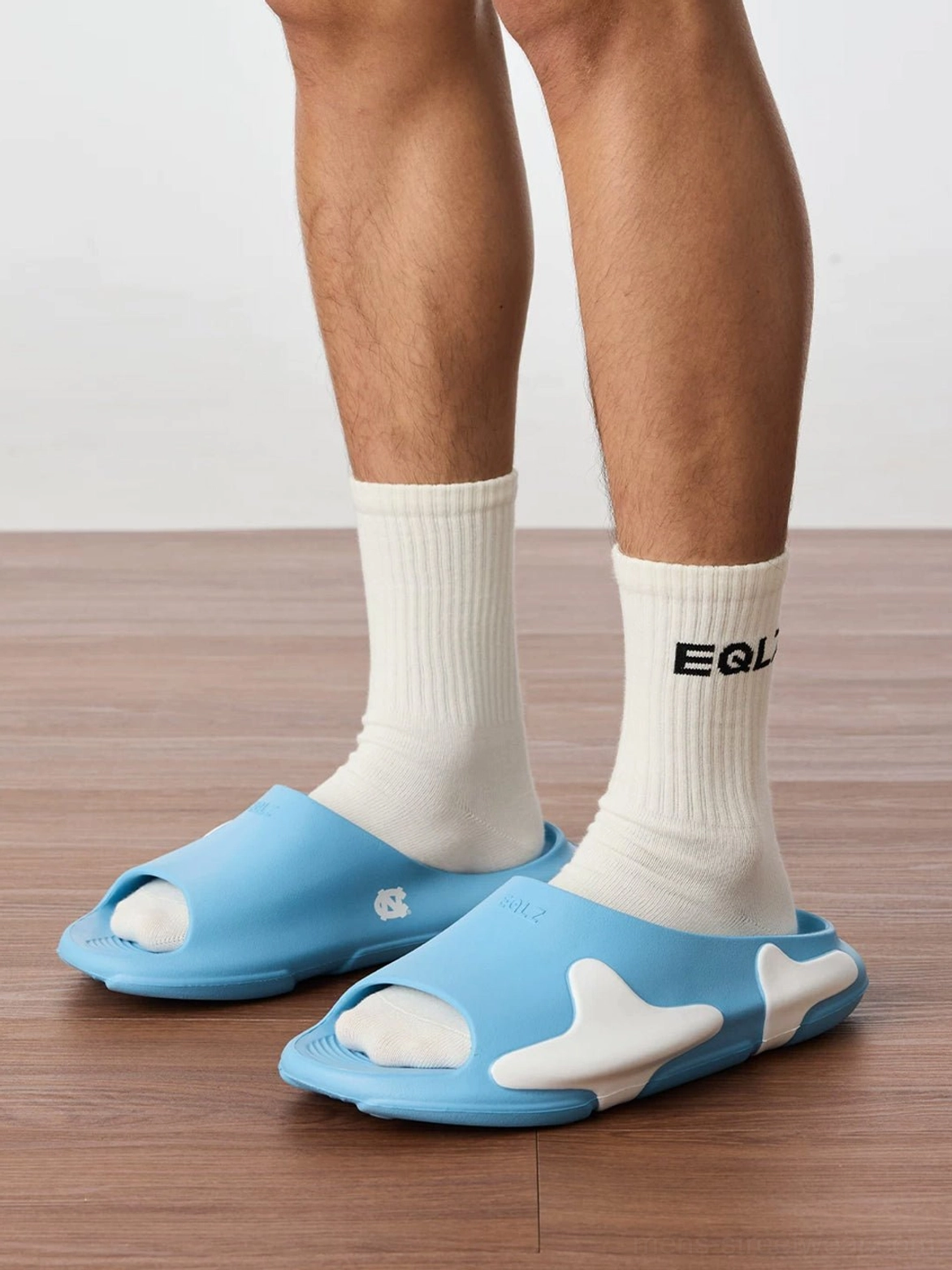 Blue and white open-toe streetwear slides worn with crew socks in a casual indoor outfit