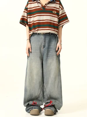 Front full-body view of blue wide-leg denim jeans with bold red triple-stripe details at the outer leg seams, styled with a striped polo shirt and casual shoes