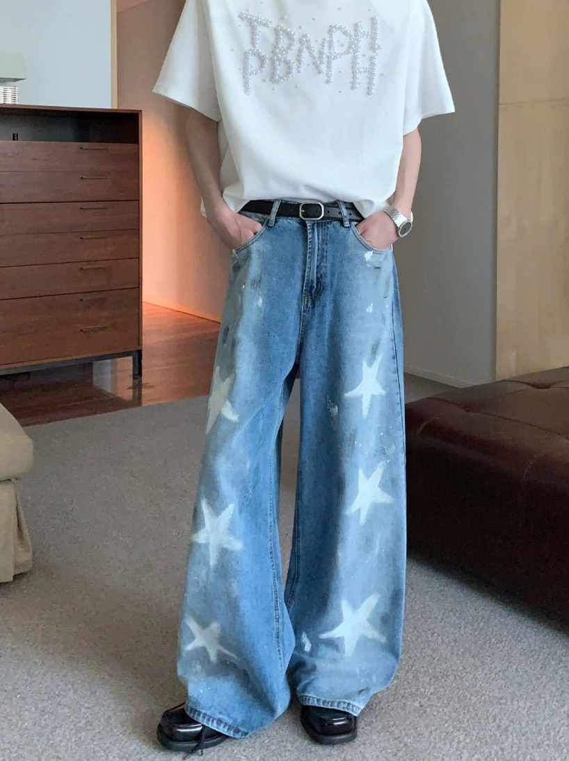Male model wearing blue wide-leg star print washed denim jeans with white graphic stars in a streetwear outfit front view