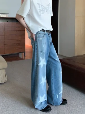 Side view of blue washed wide-leg denim jeans with white star print worn with black leather shoes in an indoor streetwear look
