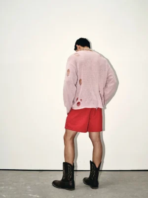 Back view of a blush pink oversized distressed knit sweater showing frayed holes, worn knit texture, and relaxed streetwear proportions