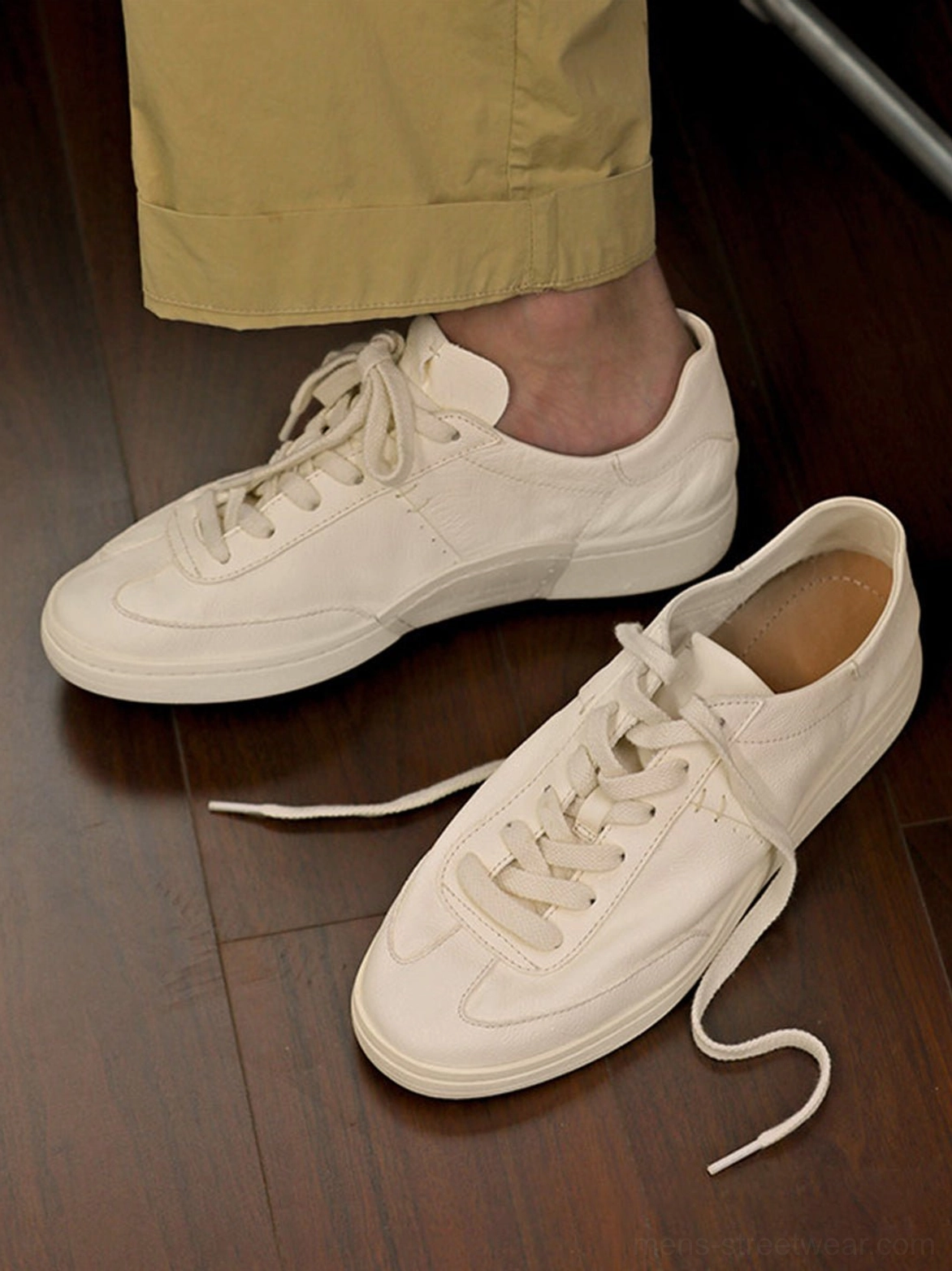 Broken-in cream leather sneaker worn with casual trousers beside a matching shoe, highlighting the relaxed low-profile everyday fit