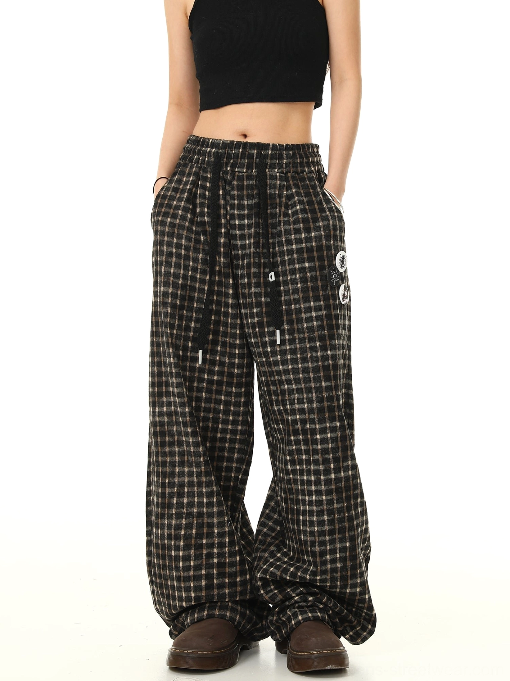 Front view of brown black check print wide leg track pants with graphic leg badges worn with a black crop top and platform shoes