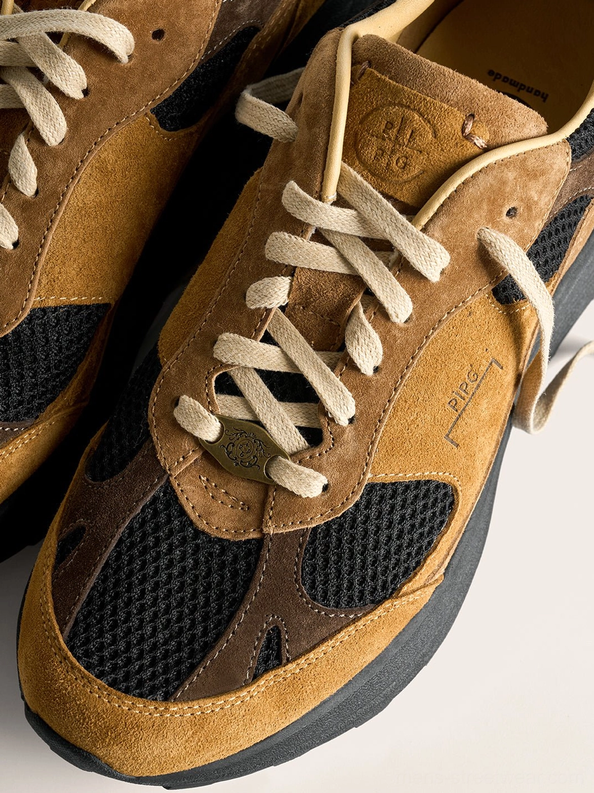 Close-up of brown and black distressed suede trail runner sneaker with cream laces layered upper and mesh panels