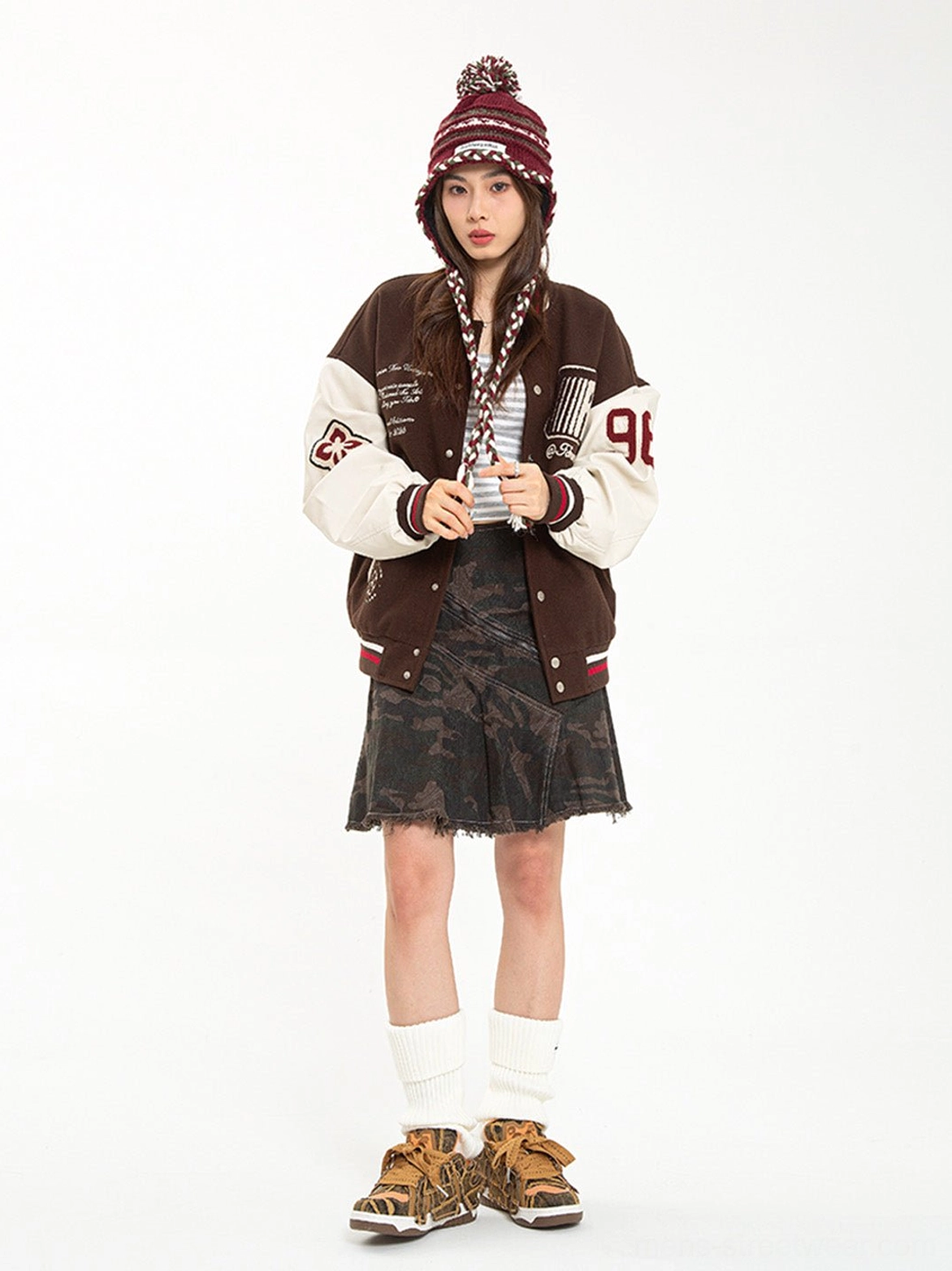 Female model wearing brown camouflage rivet platform skate sneakers with a vintage varsity jacket denim skirt and beanie