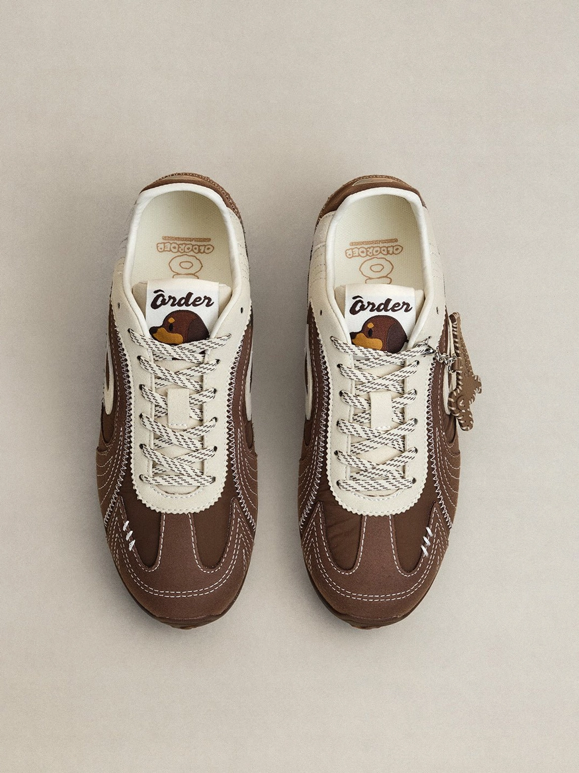 Pair of brown and cream retro trainers displayed from above with white laces, swirl panels and dog pendant