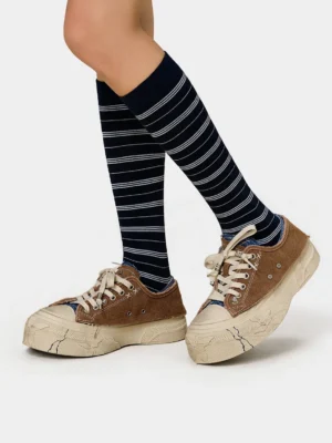 Brown distressed platform sneakers worn with navy striped knee high socks in a low angle streetwear outfit view