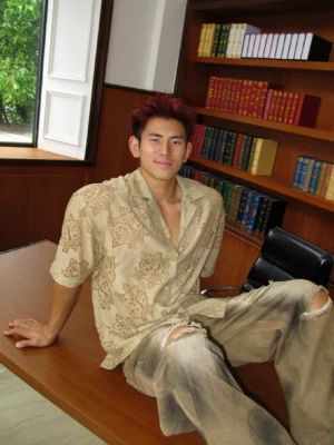 Brown floral sheer short sleeve camp shirt worn open with wide leg streetwear trousers in a vintage office setting